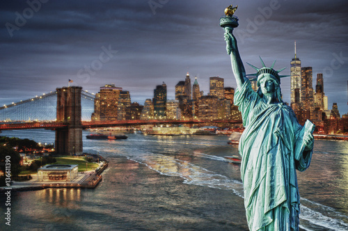Manhattah skyline with Brooklyn Bridge at night and Statue of Liberty.