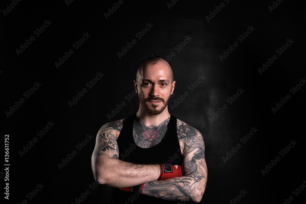 Brutal strong man with tattoo on black background. Muscular kickboxer portrait. Athletic guy in bandages before boxing. Fitness concept for advertising goods. Stock Photo