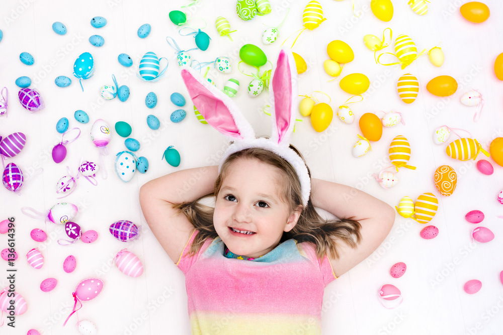 Child on Easter egg hunt. Pastel rainbow eggs.