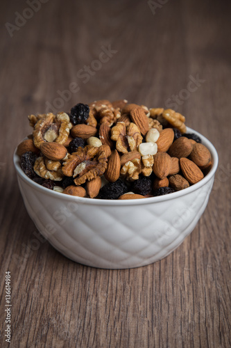 Assorted nuts in white bowl on wooden surface.