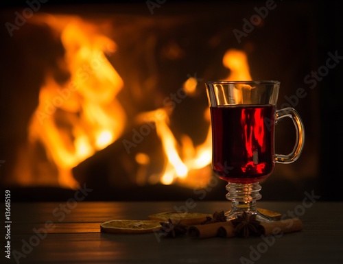 Cup of hot wine in front of fireplace on wooden table.