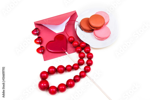 Open red envelope, wooden beads, lollipop in the shape of a heart and macarons on the white background.