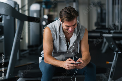 Young handsome man in sportswear using his smart phone while having rest in gym