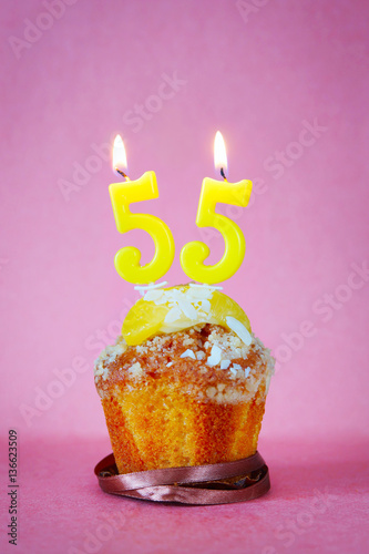 Muffin with burning birthday candles as number fifty five on pink background