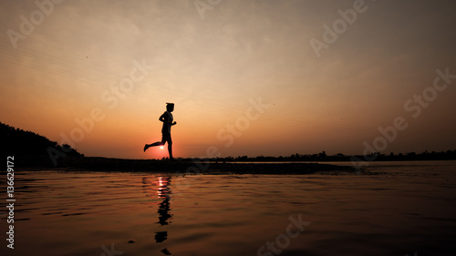 Silhouette of woman running in the morning on lake coast.