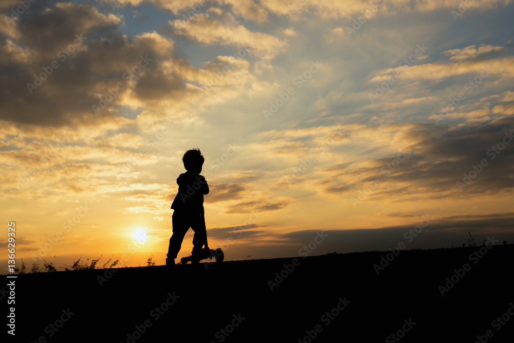 silhouette of a boy,little boy riding scooter at sunset time