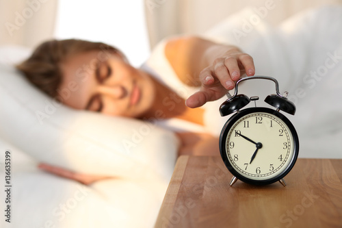 Sleepy young woman stretching hand to ringing alarm willing turn it off. Early wake up, not getting enough sleep, getting work concept.