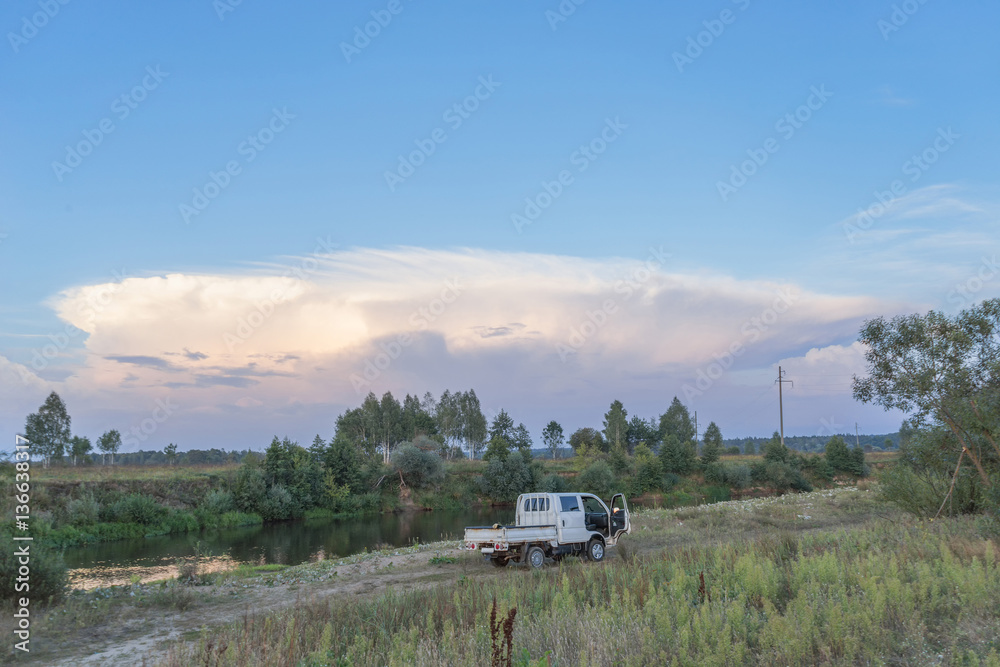 View on riverside with pik-up and big cloud in sky at sunset. Bulatovo village, Kaluzskaya region, Russia.
