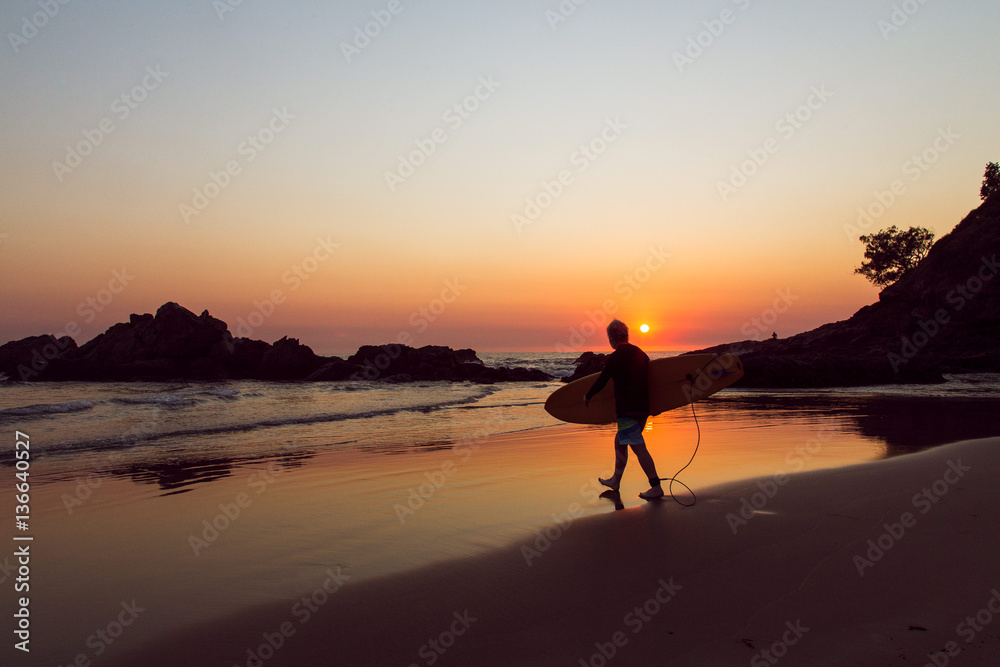 Surfer walking on the beach to the water at sunrise