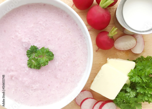 Vegetable radish soup. Cream radish soup surrounded by ingredients - radishes, butter, cream and green parsley. Wooden background. Top view.