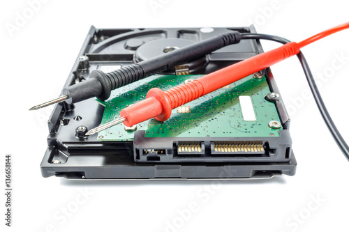 Hard disk drive with multimeter probes on a white background