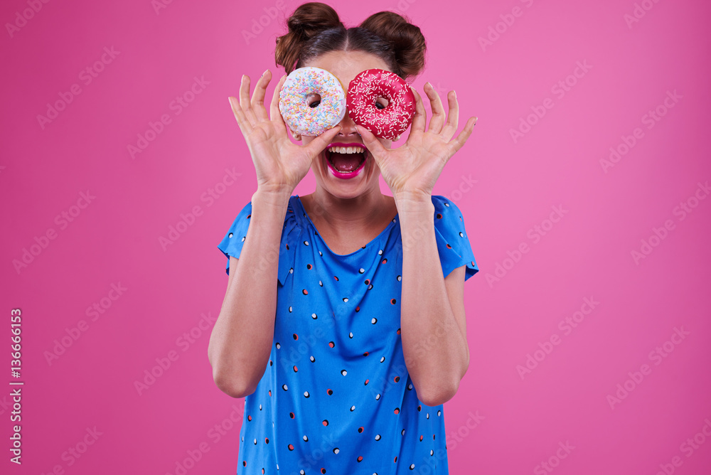 Merry woman looking through two sprinkled donutnuts