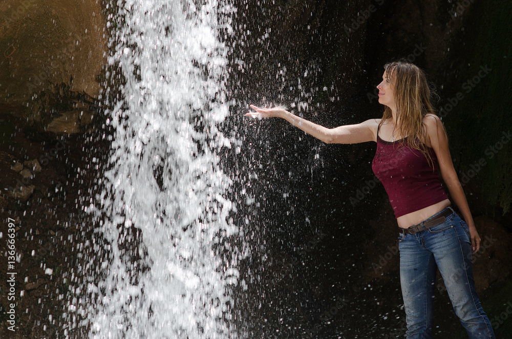 Fototapeta premium Wet woman put her hand in waterfall's water and enjoying