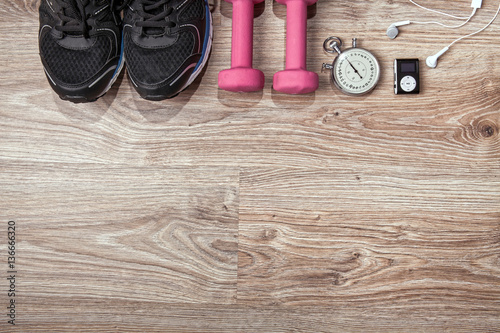 Fitness gym and running equipment. Dumbbells and running shoes, analog stopwatch and music player. Time for fitness and run. Sport accessories on the wooden floor.