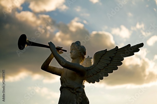 Εκτύπωση καμβά silhouette of angel blowing golden horn during sunrise against dramatic sky