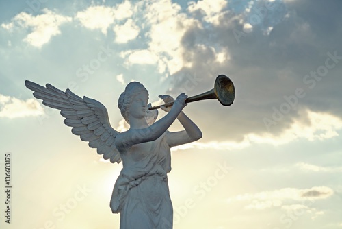 sculpture of angel blowing golden horn on sunrise sky clouds. photo