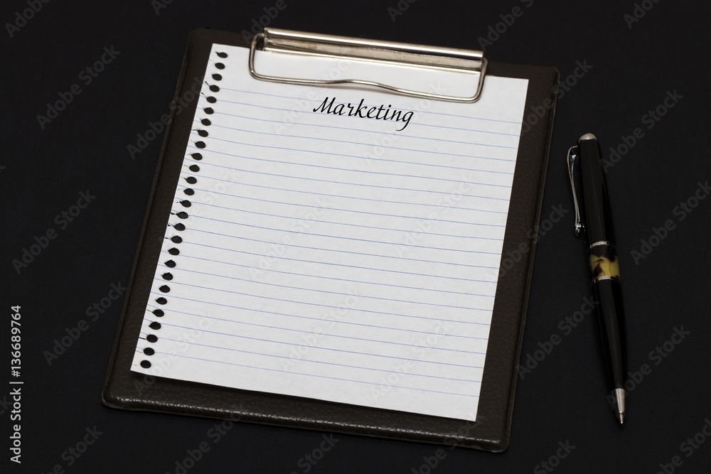 Top view of clipboard and white sheet written with Marketing on Top view of clipboard and white sheet written with Marketing on