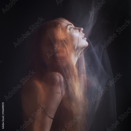 Fototapeta Beautiful model with red hair posing behind a black fabric and a veil in a studi