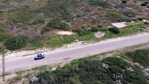 A white car is driving along the road in the desert.