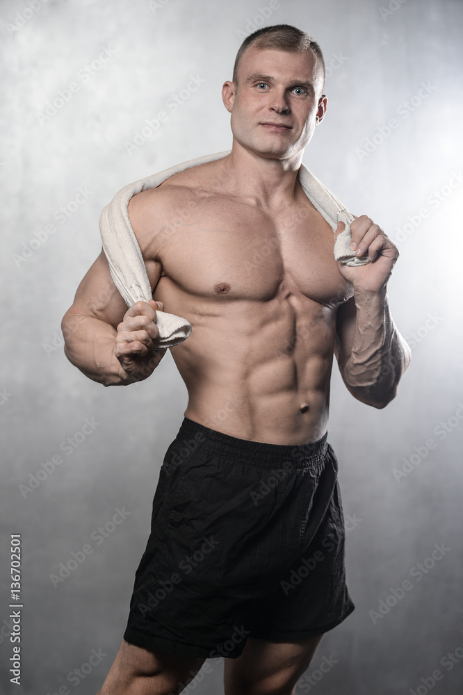 Brutal strong bodybuilder man posing in studio on grey backgroun