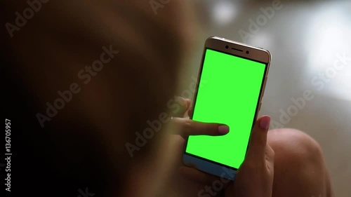 Blonde teenage girl holding a smartphone with green screen in portrait mode in daylight.
