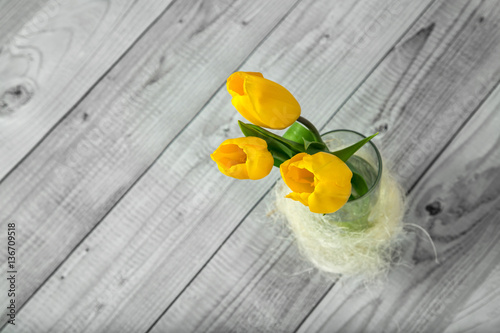 bouquet of yellow tulips in a simple glass vase on a gray background