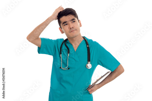 thoughtful young male doctor in uniform with stathoscope posing isolated on white background