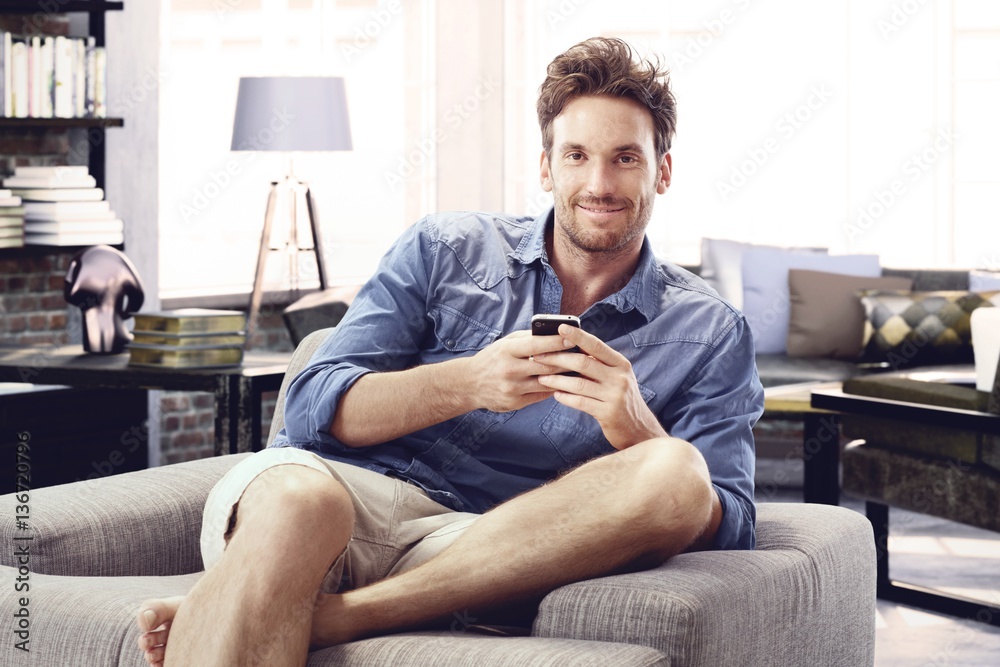 Happy man at home sitting using mobile phone