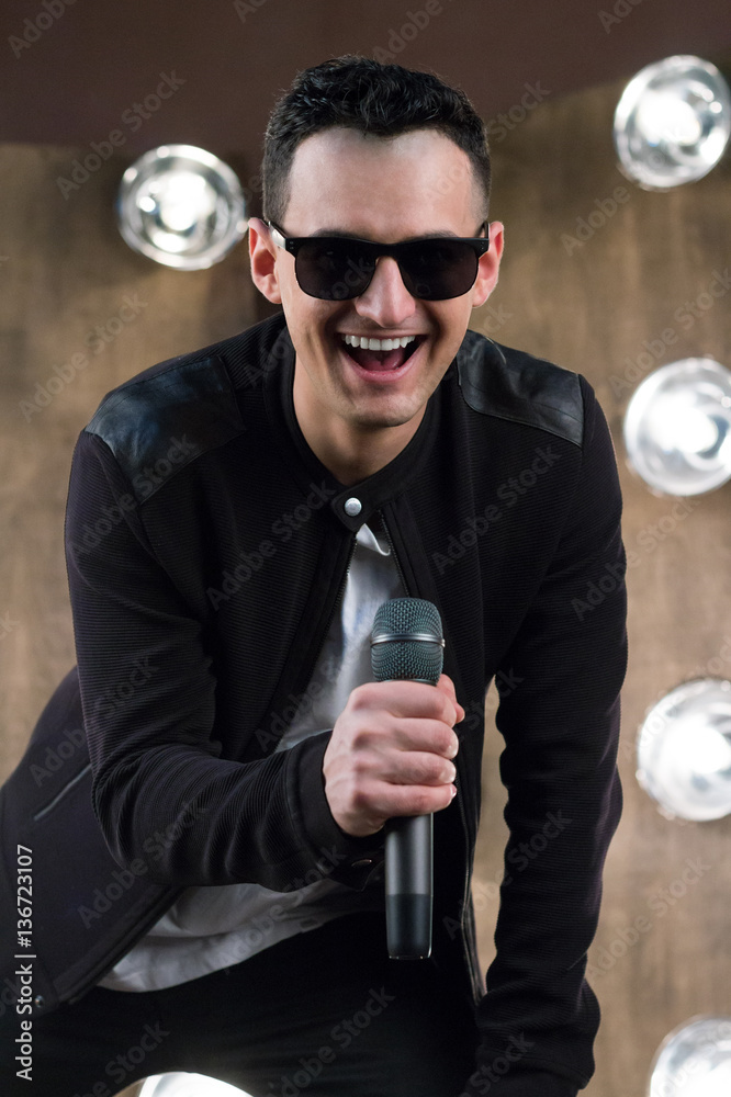 Fototapeta premium Male singer in sunglasses with microphone sings in projectors li