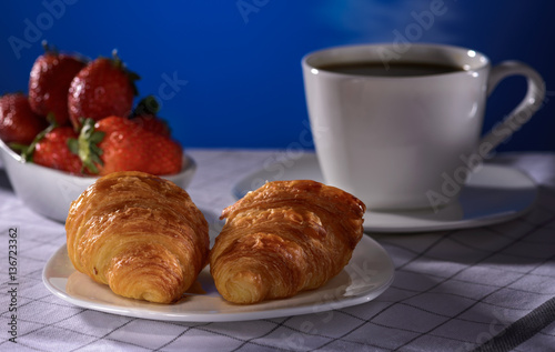 Croissants with coffee and strawberry on a blue background