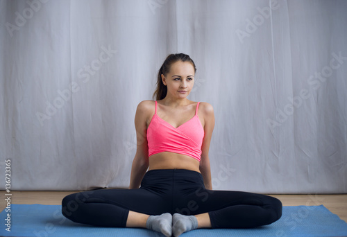 Young girl in a pink shirt performs gymnastic workout. She does it on to the mat for yoga.