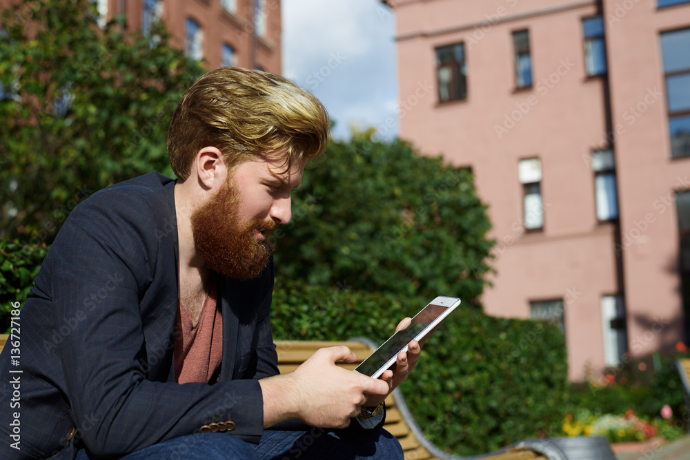 Hipster have relax time outdoor with surfing internet on europe street in old town. Technology concept. Man chat with friends through laptop or tablet.