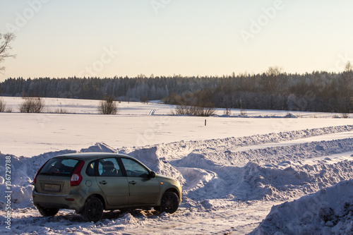 car on a rural road on the background of snow-covered field clear winter day