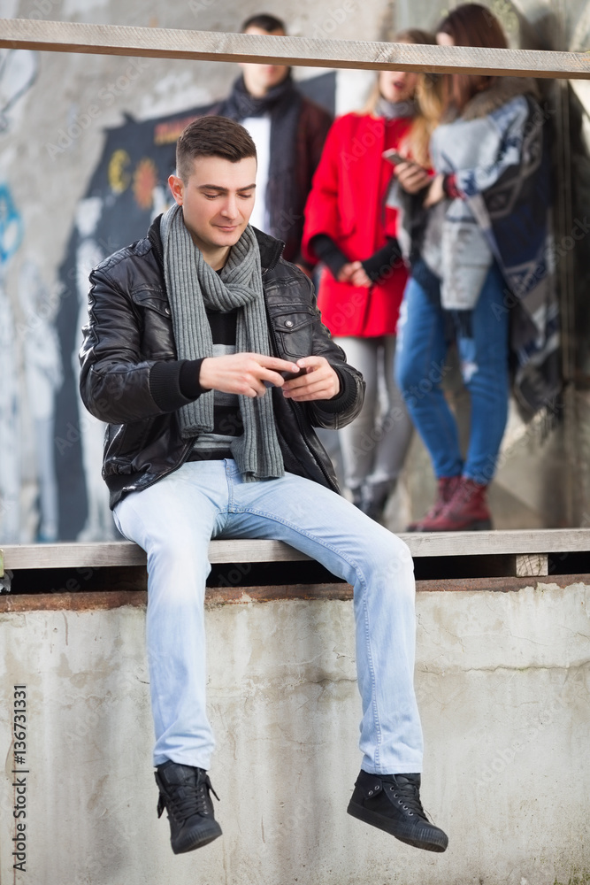 Young man texting outdoors on a wooden balcony Young man texting outdoors on a wooden balcony