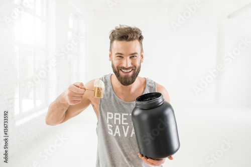 Athletic man in sportswear pouring with scooper protein powder in the white gym interior
