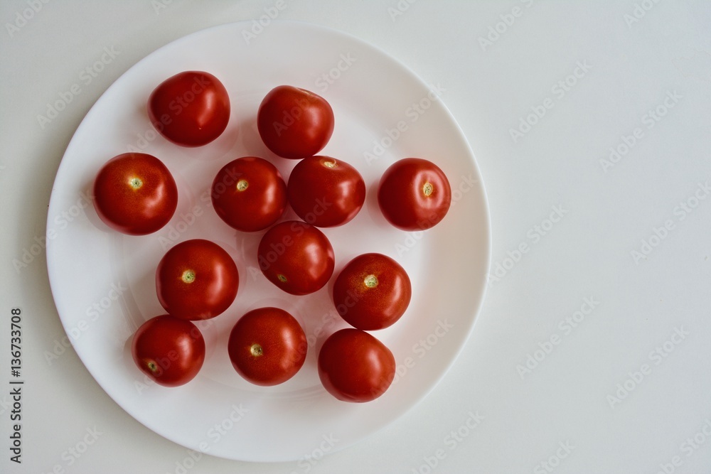 Red tomato on the white plate on the white table