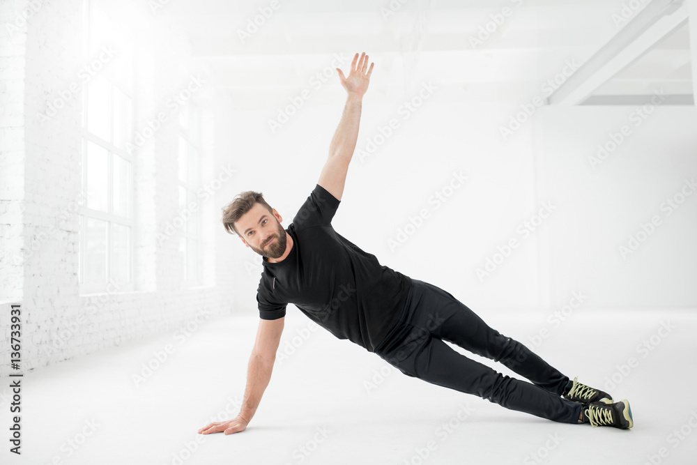 Fototapeta premium Handsome man in the black sportswear holding plank on the floor in the white gym interior