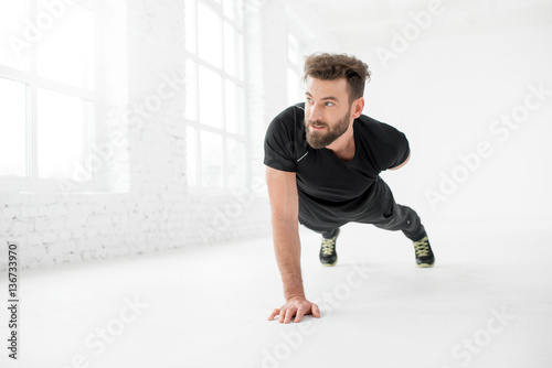 Handsome man in the black sportswear holding plank in the white gym interior