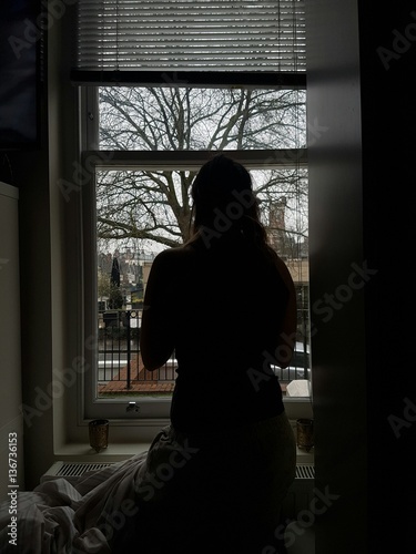 woman looking at the window whilst is snowing outside
