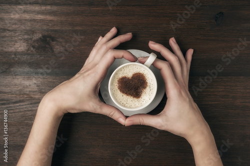 Female hand hold coffee cup with heart shape on wooden table