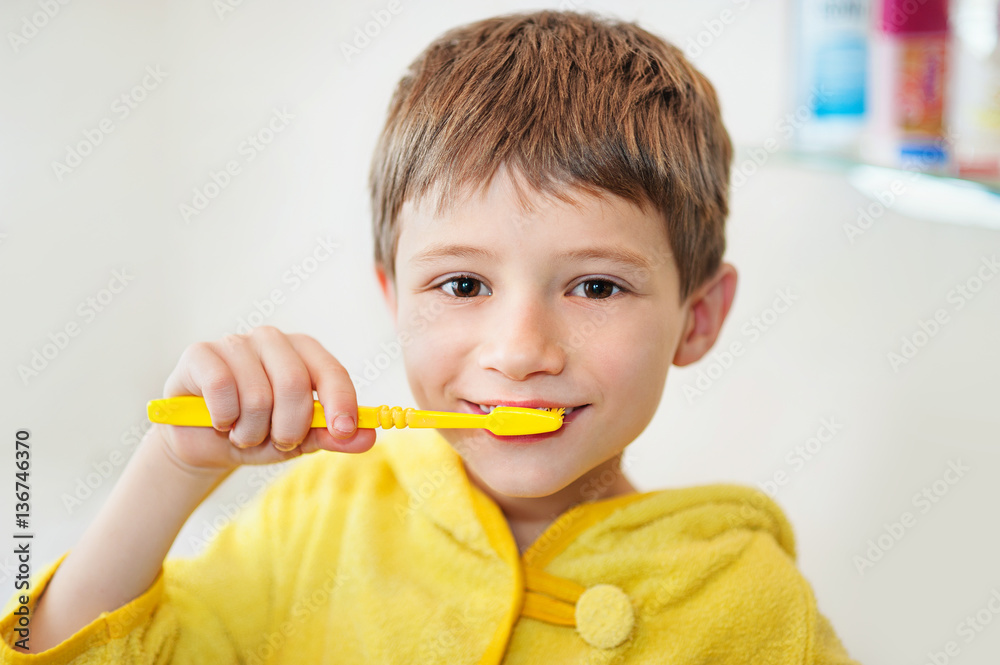 Boy brushing his teeth in bathtub, smiling, light grey background Boy brushing his teeth in bathtub, smiling, light grey background