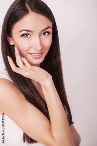 beauty, people, skincare and cosmetics concept - happy young woman with moisturizing cream on hand and facial