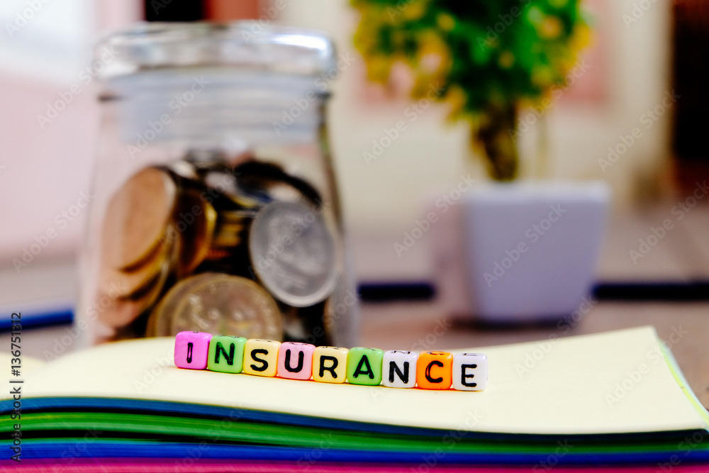 conceptual image with INSURANCE word block on note pad.coin in glass jar with soft focus background conceptual image with INSURANCE word block on note pad.coin in glass jar with soft focus background