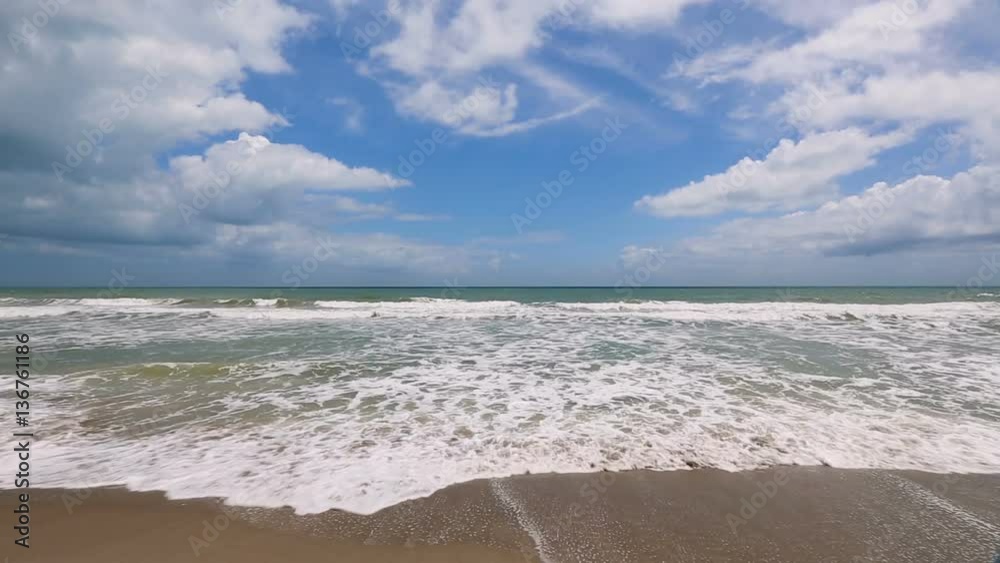 Loop features foamy gentle waves breaking on a sandy beach under a beautiful cloudy blue sky at Cocoa Beach, Florida.