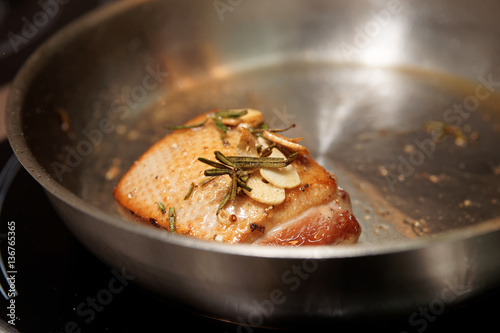 Duck breast being fried in pan with herbs