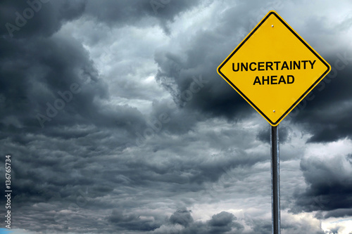 road warning sign with text uncertain ahead in front of storm cloud background photo