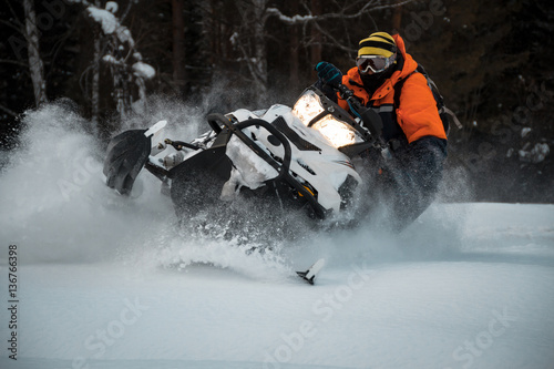 Boy athlete performs professional figure on a snowmobile in the winter forest