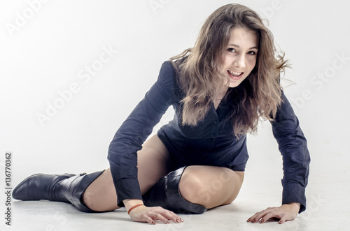 Young girl with curly hair sits gracefully coquettish in a dark shirt and high boots with heels
