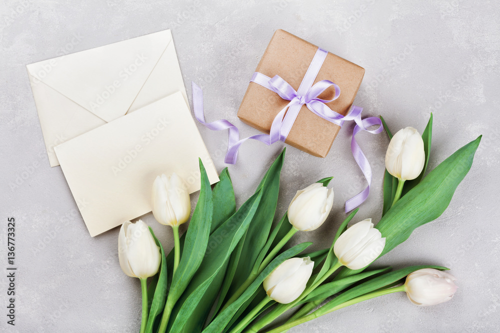 Spring tulip flowers, gift box and paper card on gray stone table top view in flat lay style. Greeting for Womens or Mothers Day. Spring tulip flowers, gift box and paper card on gray stone table top view in flat lay style. Greeting for Womens or Mothers Day.