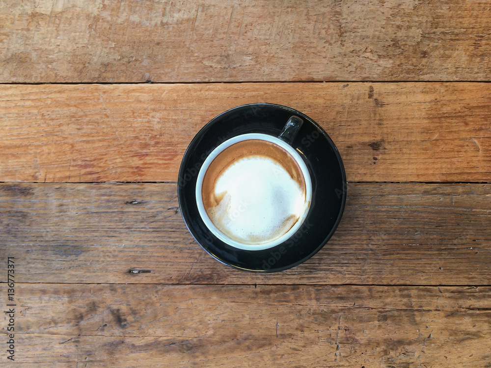 Cup of cappuccino / latte hot coffee in black cup on wooden table Cup of cappuccino / latte hot coffee in black cup on wooden table